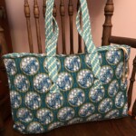 Blue and yellow patterned tote bag with decorative motifs hangs on a wooden chair.