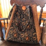 A patterned textile tote bag with a wooden button clasp, resting on a carved wooden chair in a sunlit room.