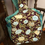 Floral-patterned fabric bag with blue and green accents hanging on a wooden chair.