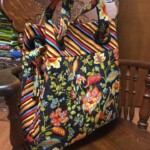 A large floral and striped tote bag sits on a wooden chair, with stacks of fabric visible in the background.