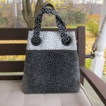 Black and white polka dot handbag on a wooden bench, outdoors with fallen leaves and trees in the background.