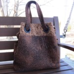 Brown leopard print handbag with black handles resting on a wooden bench outdoors.
