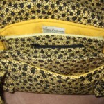 A yellow and black floral-patterned fabric bag with an open flap, revealing multiple compartments and a zippered pocket inside.