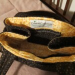 A fabric handbag with a yellow floral interior lining and a label from Creative Craftworks on the inside pocket.