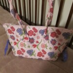 A floral-patterned handbag with pink, purple, and red flowers, resting on a beige surface.