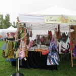 Outdoor craft booth displaying a variety of handmade bags under a white tent, with trees in the background.