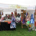 Craft booth displaying various handmade bags and accessories under a white canopy with a "Creative Craftworks" sign.