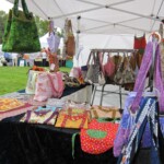 Tent with handmade bags and fabrics displayed on tables at an outdoor market.