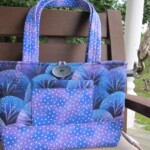 A purple tote bag with a tree pattern and a front pocket, featuring polka dots, is placed on a wooden chair outdoors.