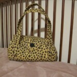 Yellow and black floral-patterned handbag on a beige quilted surface near wooden bars.