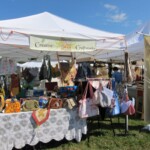 Outdoor craft fair booth displaying various handmade bags under a white canopy.
