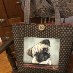 Tote bag with a polka dot design and a painted image of a pug, placed on an intricately carved wooden chair.