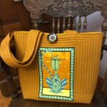 Yellow quilted tote bag with a floral and cat design on the front, displayed on a wooden chair.