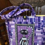 Purple plaid handbag with a cartoon cat design on the front, displayed on a wooden chair with ornate carving.
