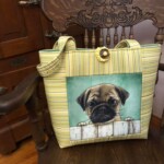 A yellow striped tote bag with a pug design sits on a wooden chair with ornate carvings.