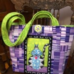 Purple and green fabric tote bag with a whimsical cat design sits on a wooden chair.
