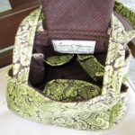 Green and brown patterned fabric purse with a label reading "Creative Craftworks" displayed on a chair.