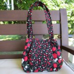 A floral-patterned handbag with red, white, and green flowers sits on a bench outdoors.