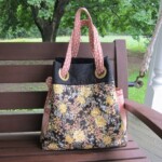 A floral-patterned tote bag with pink polka dot handles rests on a wooden bench outdoors.