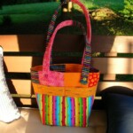Colorful handmade tote bag with striped, patchwork patterns rests on a wooden bench next to striped and dark cushions.