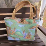A fabric tote bag with colorful illustrations of cartoon animals sits on a wooden swing.