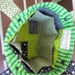 Top view of an open fabric bag with green and black geometric patterns, showing a multicolored interior and two handles.
