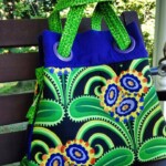 A colorful tote bag with a vibrant green, yellow, and blue floral pattern, featuring circular handle loops.