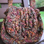 A colorful, patterned fabric bag with ruffled design rests on a wooden bench.