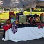 Craft fair booth with a variety of colorful handmade bags and accessories displayed under a white canopy.