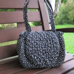 Black and white patterned handbag with two handles placed on a wooden bench outdoors.