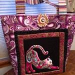 Colorful fabric handbag with a detailed pattern featuring an ornate cat design, stripes on the handle, and intricate bordering.