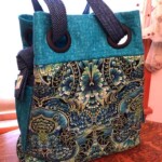 A colorful tote bag with ornate floral patterns and polka dot handles, resting on a wooden table.