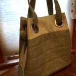 Olive green tote bag with striped and textured fabric, featuring large metal eyelets for the handles, placed on a wooden surface.