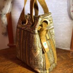 Ornate brown and beige paisley-patterned bag with large circular handles and decorative knot, resting on a wooden surface.
