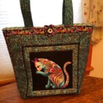 Colorful tote bag featuring an artistic, patterned cat design with paisley straps and trim on a wooden table.