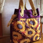 Fabric tote bag with sunflower design, purple background, and patterned handles, placed on a wooden surface.