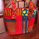 A colorful patchwork bag with a variety of geometric patterns and button details sits on a wooden chair.