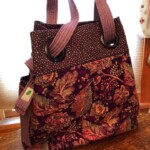 Purple floral-patterned tote bag with large grommets and thick handles, set on a wooden surface.
