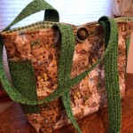 Tote bag with teddy bear pattern and green handles on a wooden table, illuminated by natural light from a window.