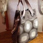 A brown and white patterned tote bag with two handles sits on a wooden table in front of a window.