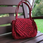 Red woven handbag with floral patterns on a wooden bench outdoors.