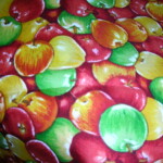 A colorful fabric pattern featuring overlapping red, green, and yellow apples.