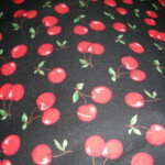 Patterned fabric with red cherries and green leaves on a black background.