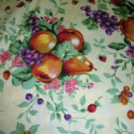 A fabric pattern featuring pears, grapes, and small flowers on a light background.