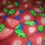 Patterned fabric with a vibrant design of large red strawberries with green leaves on a blue background.