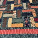 Patchwork quilt with a variety of colorful rectangular and square fabric pieces on a dark floral background.