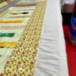 A colorful quilt with floral patterns is laid out on a quilting machine, ready for stitching in a sewing room.