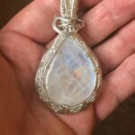 A hand holding a teardrop-shaped pendant with a wrapped wire design and iridescent center.