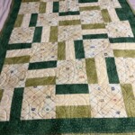 Quilt with varying shades of green and cream, featuring rectangular patterns and subtle stitched designs.