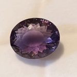 Oval-cut purple gemstone on a white background, displaying facets and color gradients.